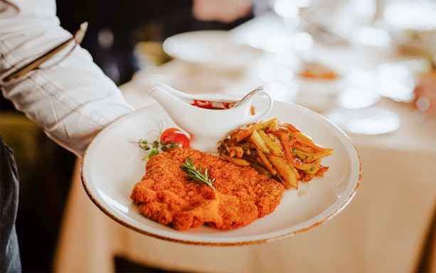 Waiter serving Viennese Schnitzel with fried potatoes and sauce.