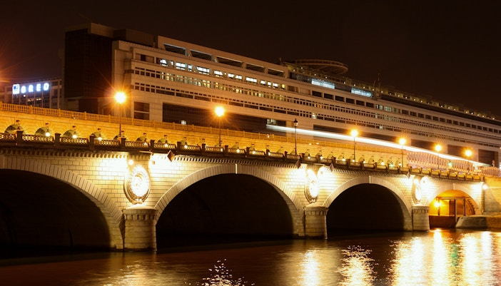 Night view of the Bibliothèque Nationale de France with illuminated bridge over the Seine River.