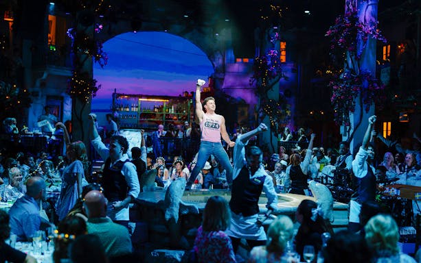 Guests enjoying a lively performance at Mamma Mia! The Party in a vibrant Greek taverna setting.