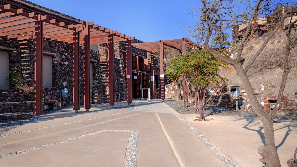 Entrance to Akrotiri Archaeological Site, Santorini, with stone walls and wooden pergolas.