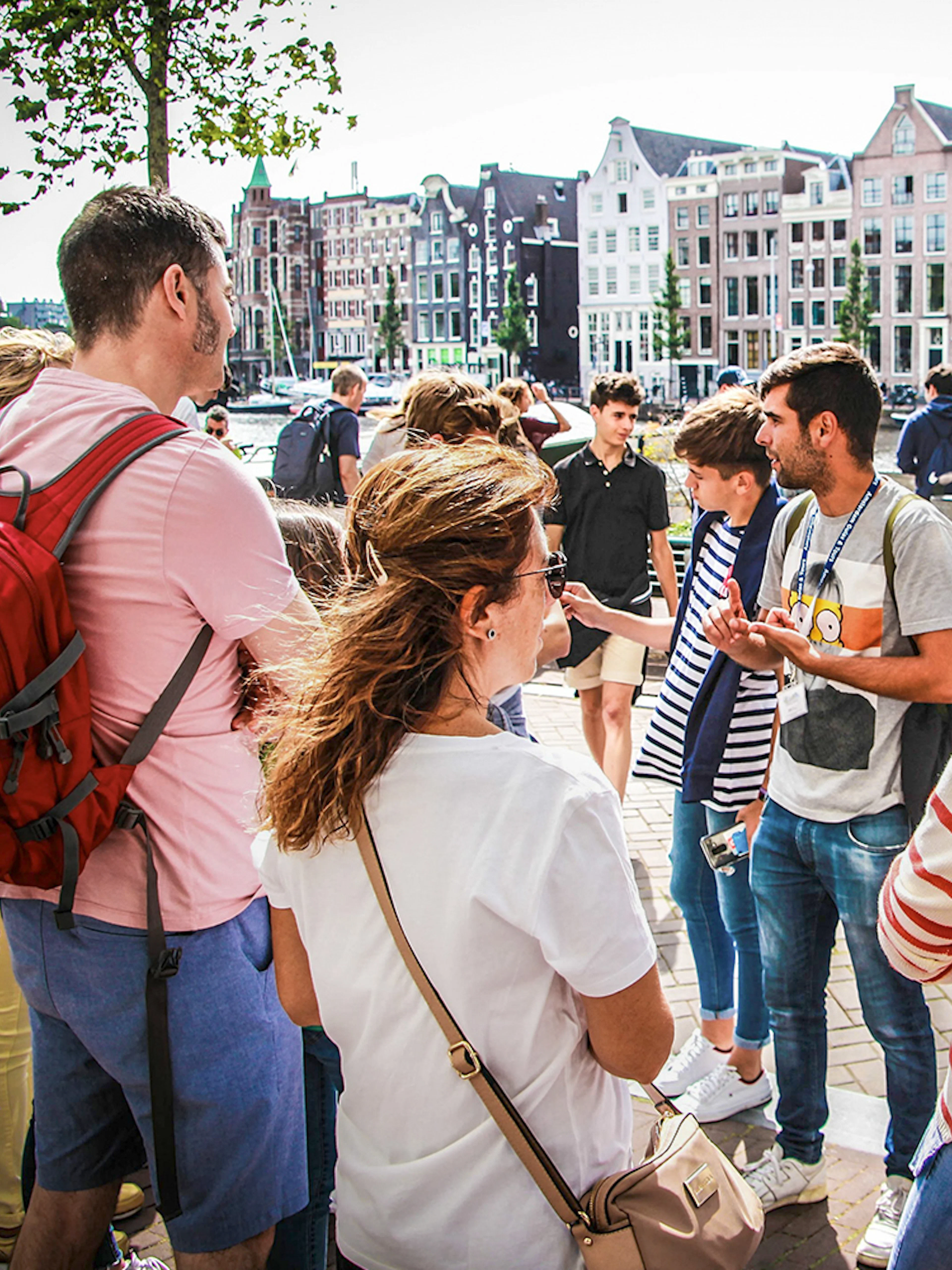 Tour guide explaining to tourists in Amsterdam with canal houses in the background.