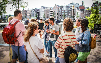 Tour guide explaining to tourists in Amsterdam with canal houses in the background.