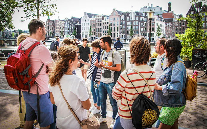 Tour guide explaining to tourists in Amsterdam with canal houses in the background.