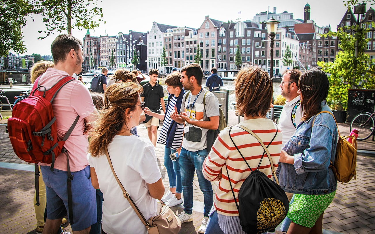 Tour guide explaining to tourists in Amsterdam with canal houses in the background.