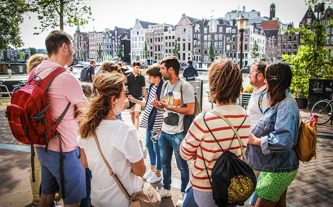 Tour guide explaining to tourists in Amsterdam with canal houses in the background.