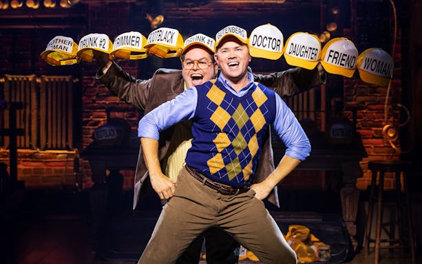 Two performers on stage in "Gutenberg! The Musical!" wearing character hats.