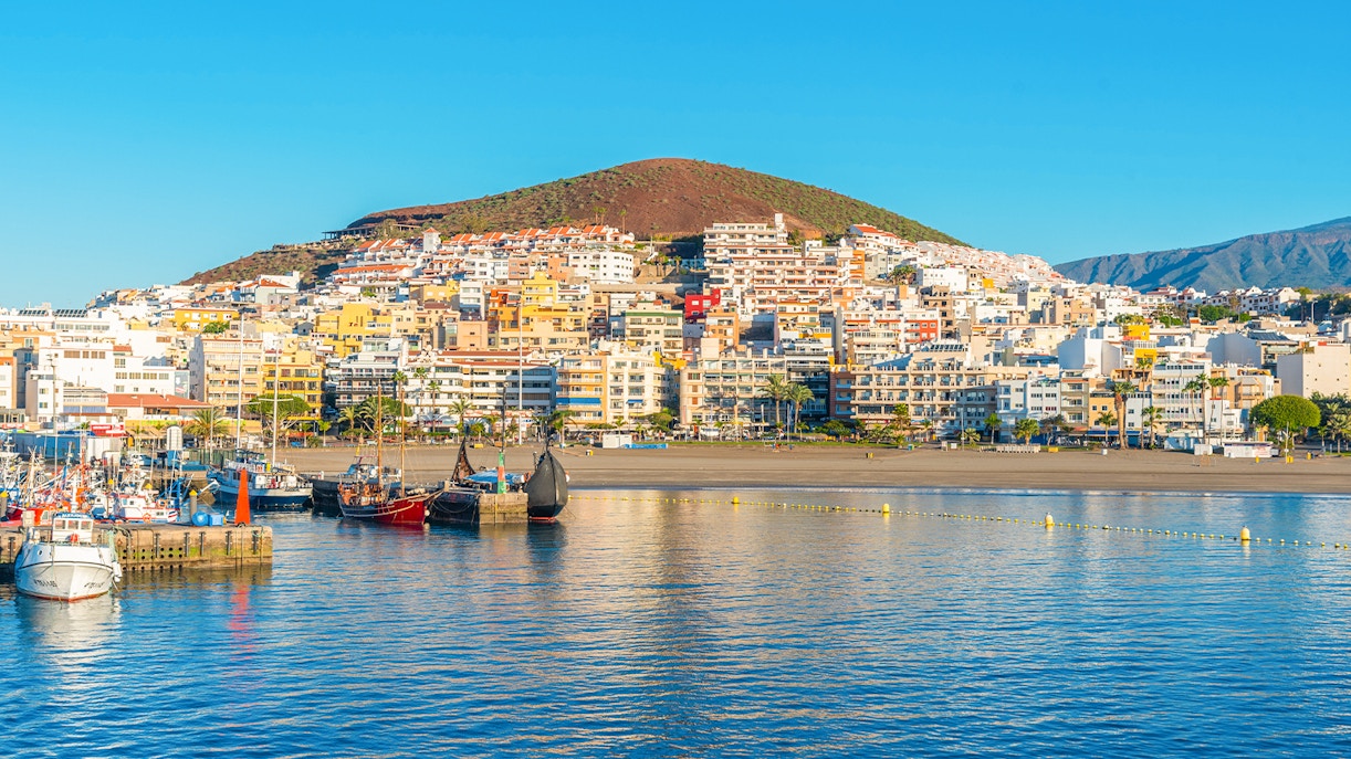 Boats docked at Playa de los Cristianos with colorful buildings and hills in Tenerife, Canary Islands, Spain.