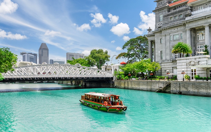 Boat cruising on Singapore River with city skyline and historic bridge in view.