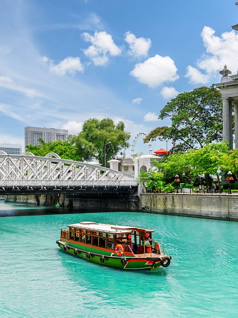 Boat cruising on Singapore River with city skyline and historic bridge in view.