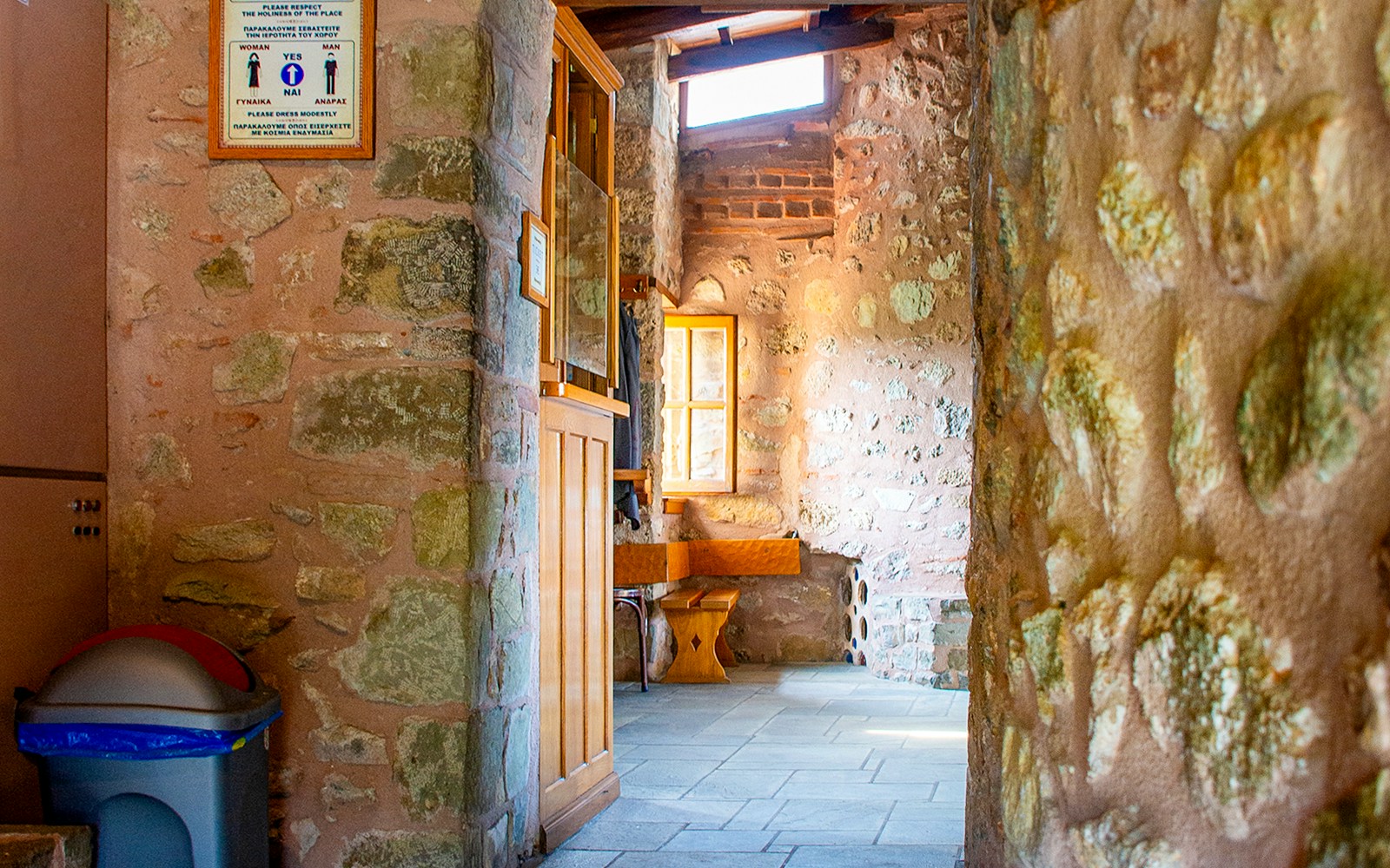 Stone hallway inside Monastery of Rousanos with wooden bench and window.