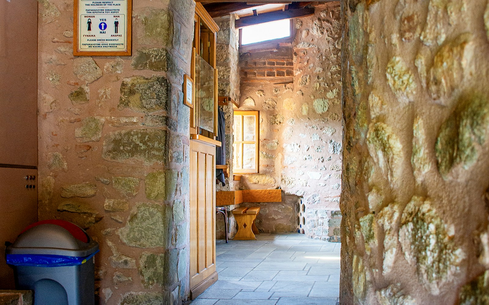 Stone hallway inside Monastery of Rousanos with wooden bench and window.