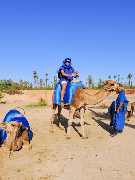 Camel ride in Palmeraie with people in blue attire, surrounded by palm trees.