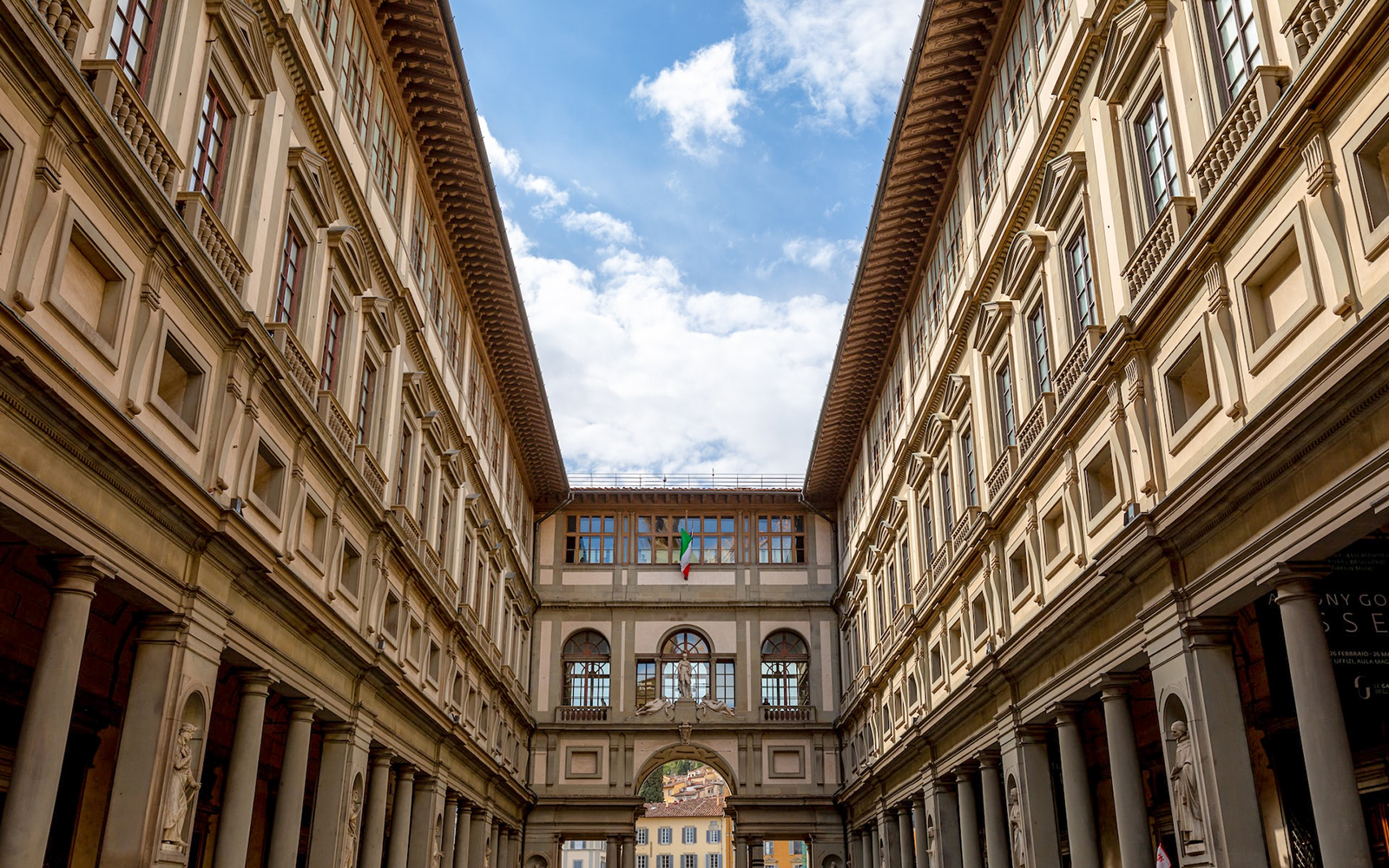 O icônico arco da Galeria Uffizi emoldura uma vista das exuberantes colinas de Florença, com estátuas de guarda, um testemunho do duradouro caso de amor da cidade com a arte