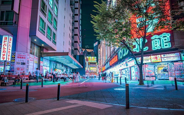Neon-lit street in Tokyo at night, bustling with people and vibrant signs.