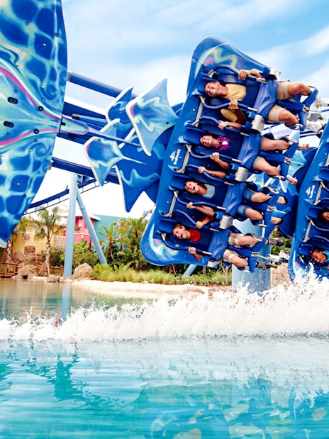 Riders on Manta roller coaster at SeaWorld gliding over water.
