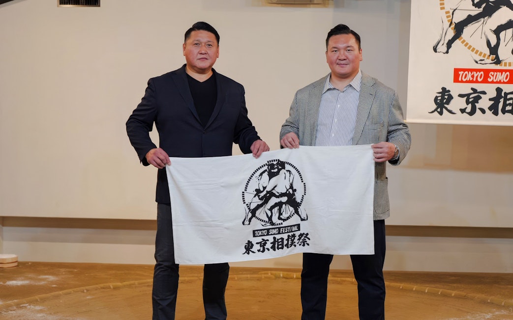 Two tourists holding a Ginza: Sumo Show banner in Tokyo.