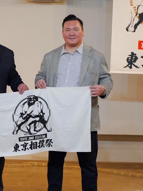 Two tourists holding a Ginza: Sumo Show banner in Tokyo.