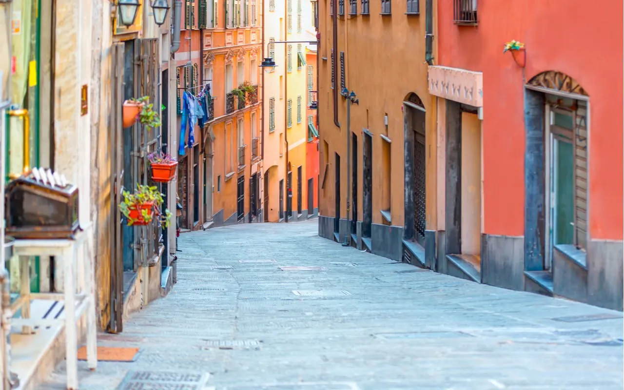 Narrow cobblestone street in Genoa with colorful buildings, part of a self-guided city exploration game.