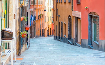 Narrow cobblestone street in Genoa with colorful buildings, part of a self-guided city exploration game.