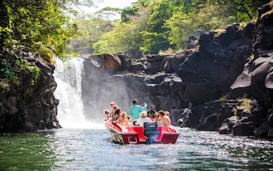 Tourists on a boat approaching a waterfall near Ile aux Cerf, Mauritius.