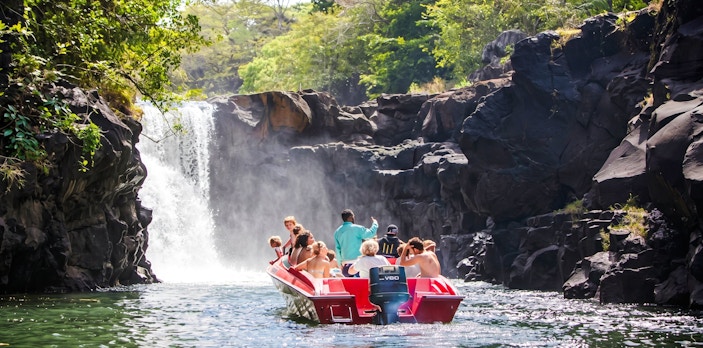 Tourists on a boat approaching a waterfall near Ile aux Cerf, Mauritius.
