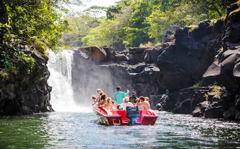 Tourists on a boat approaching a waterfall near Ile aux Cerf, Mauritius.
