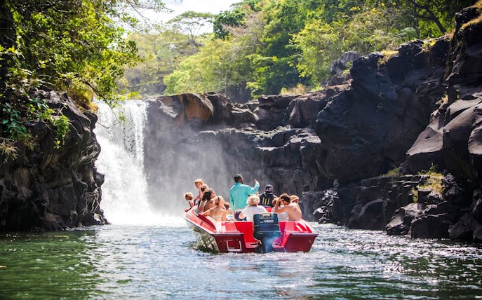 Tourists on a boat approaching a waterfall near Ile aux Cerf, Mauritius.