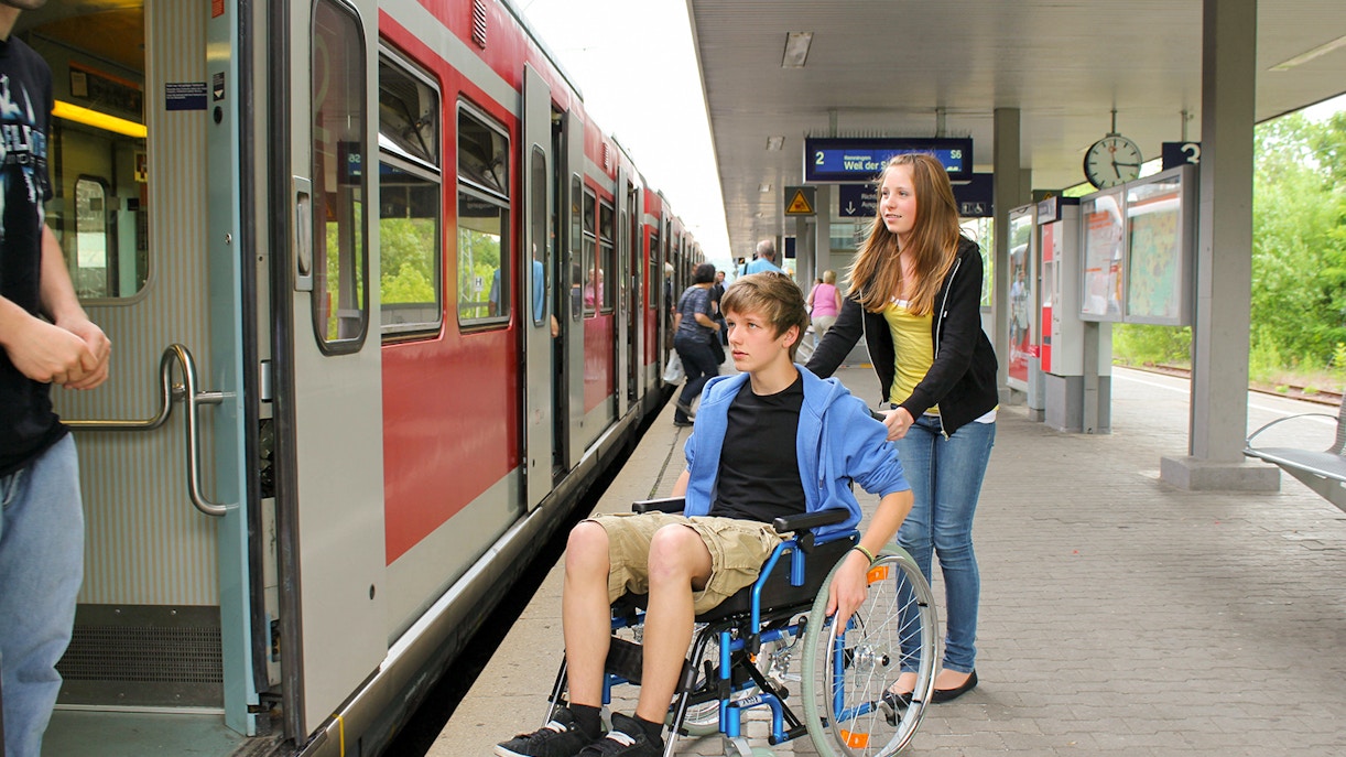 A boy on wheelchair being assisted by a woman at a station on the route of Bernina Train