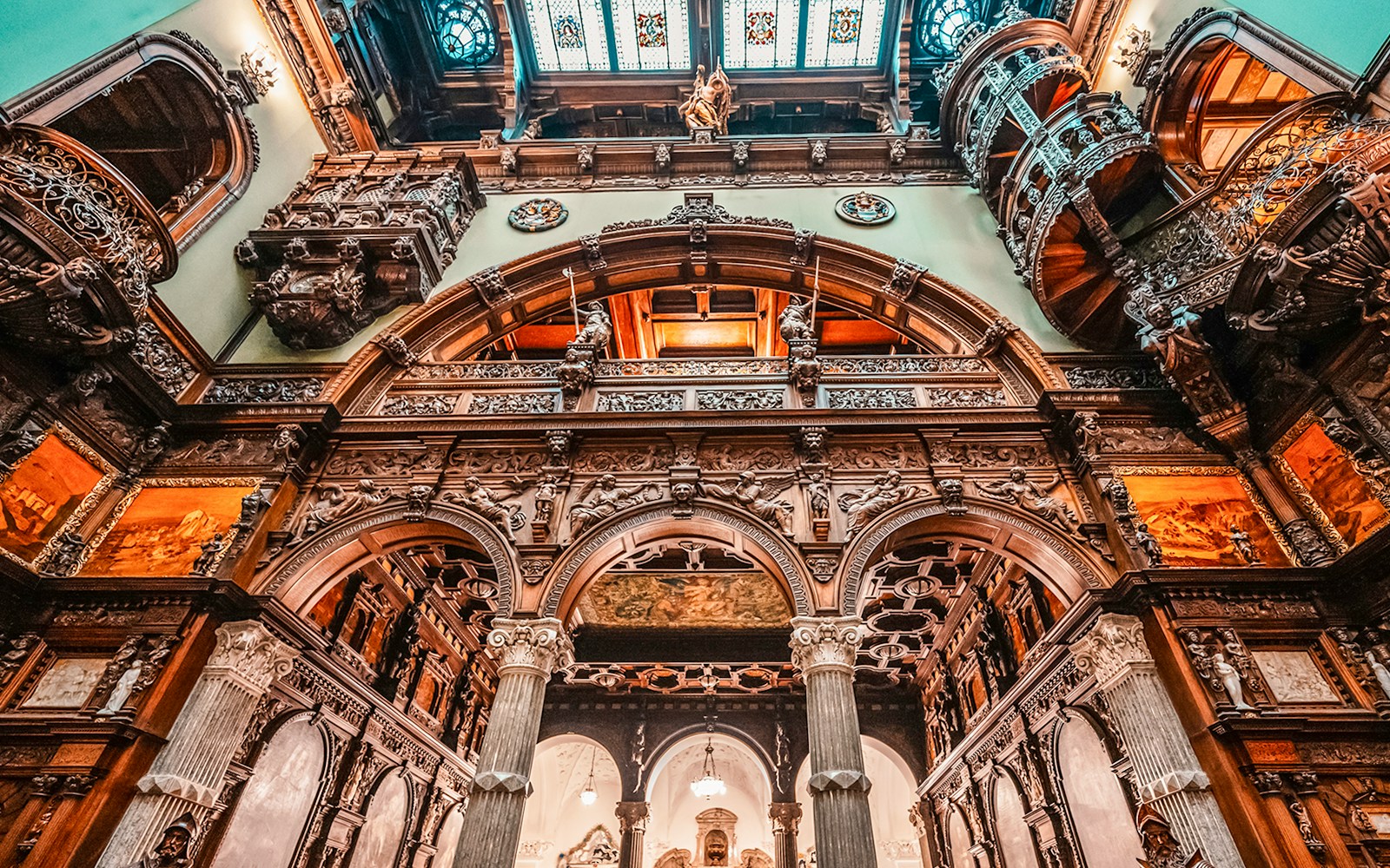 Hall stairs and Hall of Honor in Peles Castle with ornate wood carvings and arches.