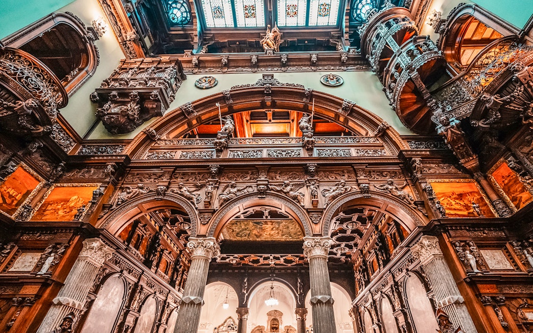 Hall stairs and Hall of Honor in Peles Castle with ornate wood carvings and arches.