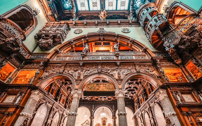 Hall stairs and Hall of Honor in Peles Castle with ornate wood carvings and arches.