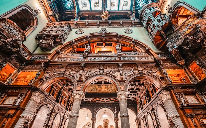 Hall stairs and Hall of Honor in Peles Castle with ornate wood carvings and arches.