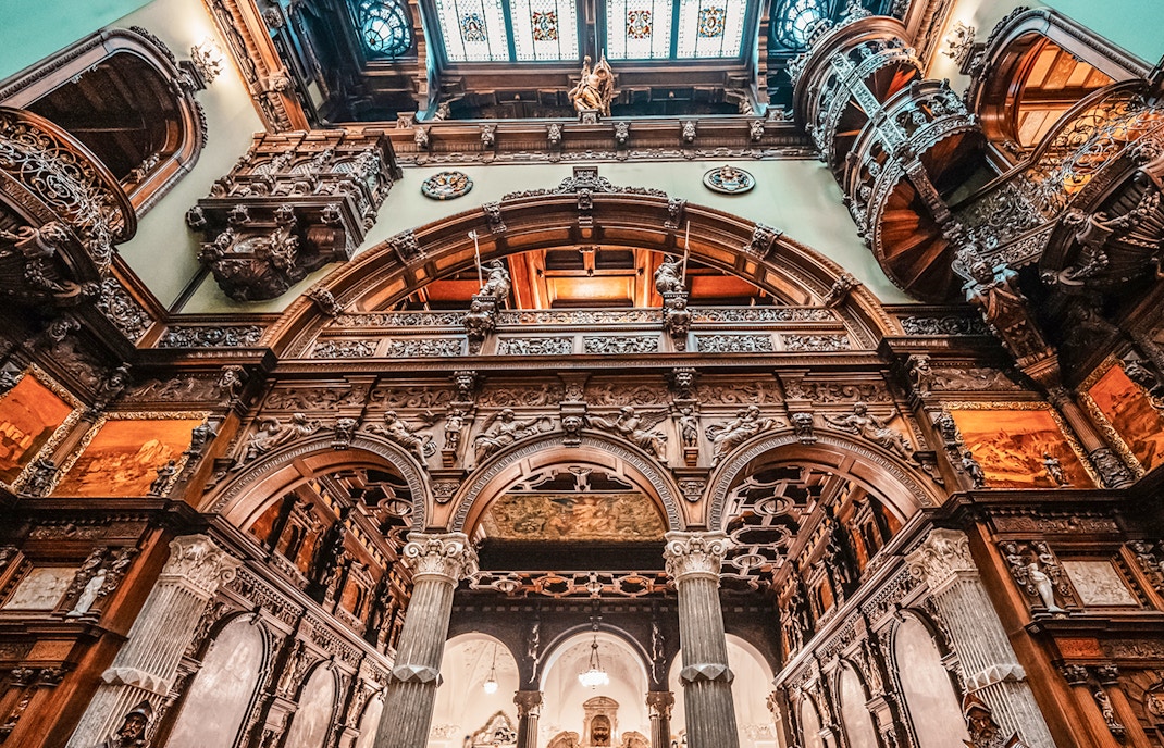 Hall stairs and Hall of Honor in Peles Castle with ornate wood carvings and arches.
