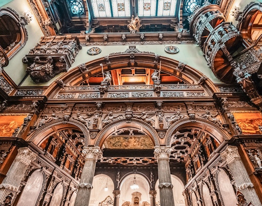 Hall stairs and Hall of Honor in Peles Castle with ornate wood carvings and arches.