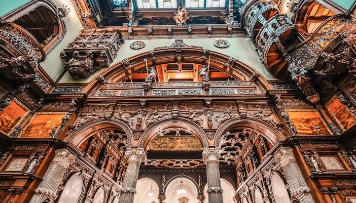 Hall stairs and Hall of Honor in Peles Castle with ornate wood carvings and arches.