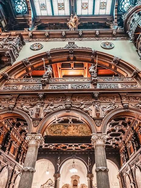 Hall stairs and Hall of Honor in Peles Castle with ornate wood carvings and arches.