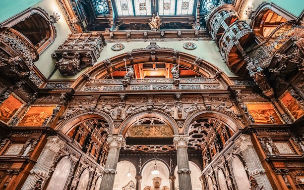 Hall stairs and Hall of Honor in Peles Castle with ornate wood carvings and arches.