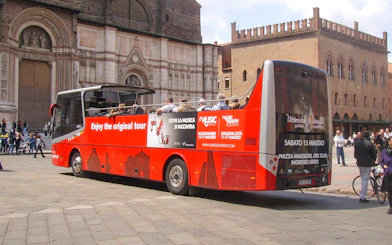 Red double-decker bus in Bologna city center, part of hop-on hop-off tour with food tasting vouchers.