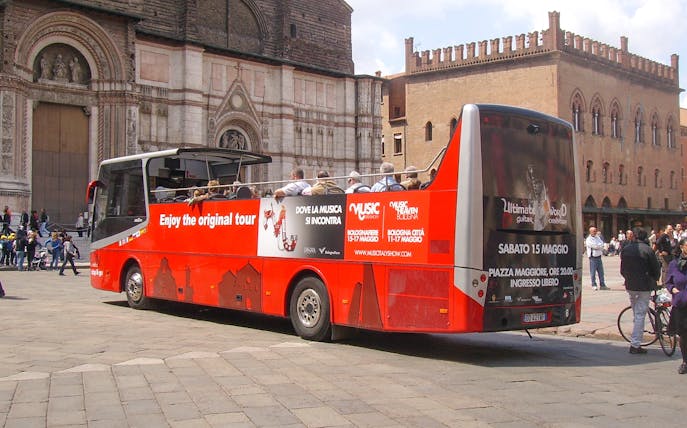 Red double-decker bus in Bologna city center, part of hop-on hop-off tour with food tasting vouchers.