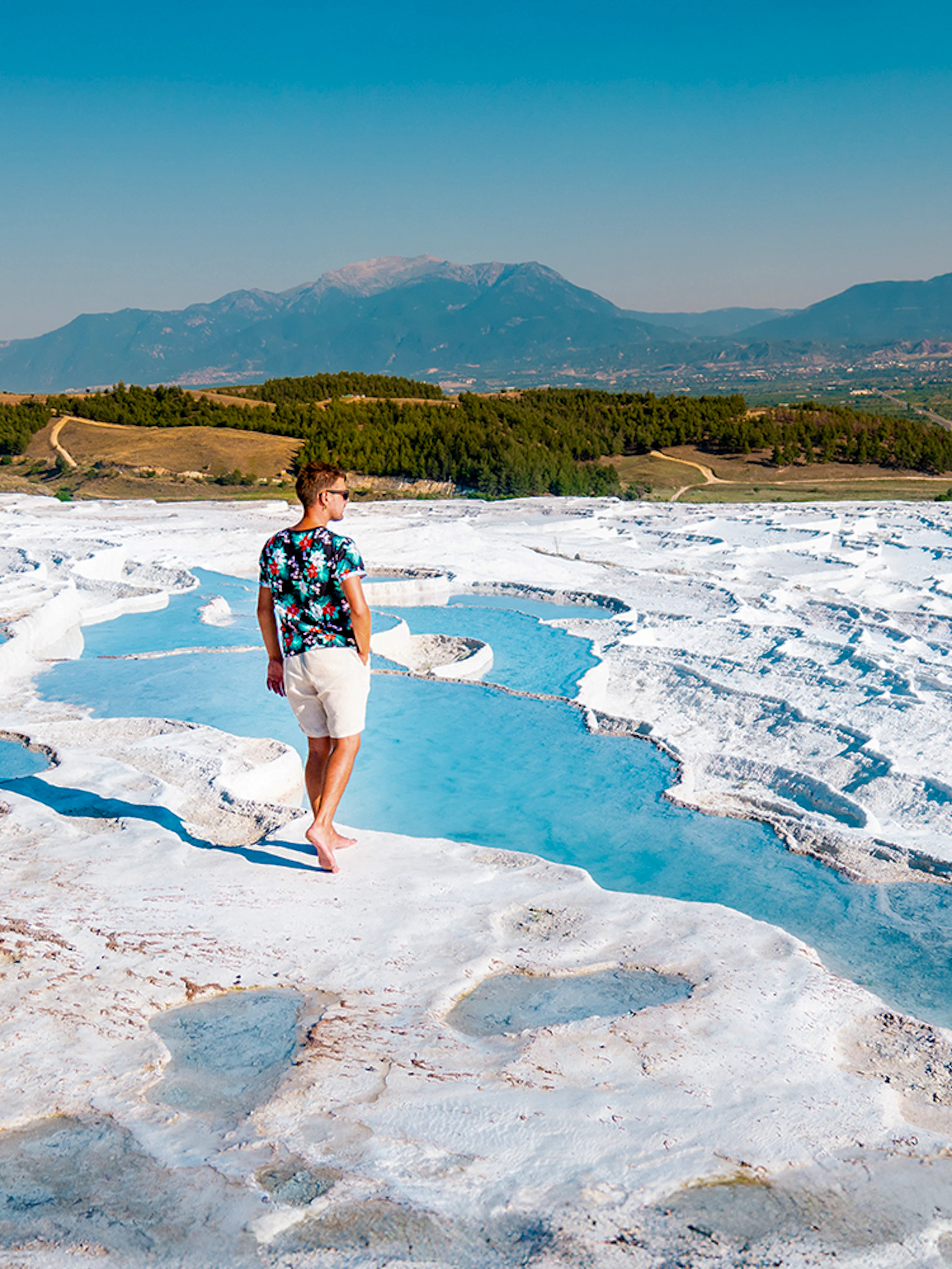 Person walking on travertine terraces at Pamukkale, Turkey, with mountains in the background.