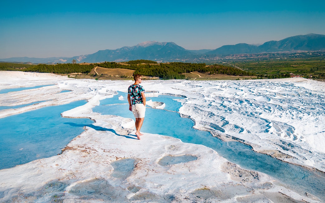 Person walking on travertine terraces at Pamukkale, Turkey, with mountains in the background.