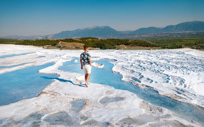 Person walking on travertine terraces at Pamukkale, Turkey, with mountains in the background.