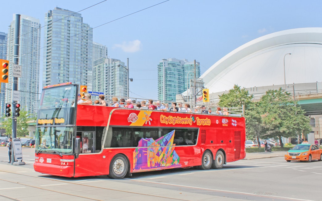 Tourists on a City Sightseeing bus exploring Toronto with CN Tower in the background.