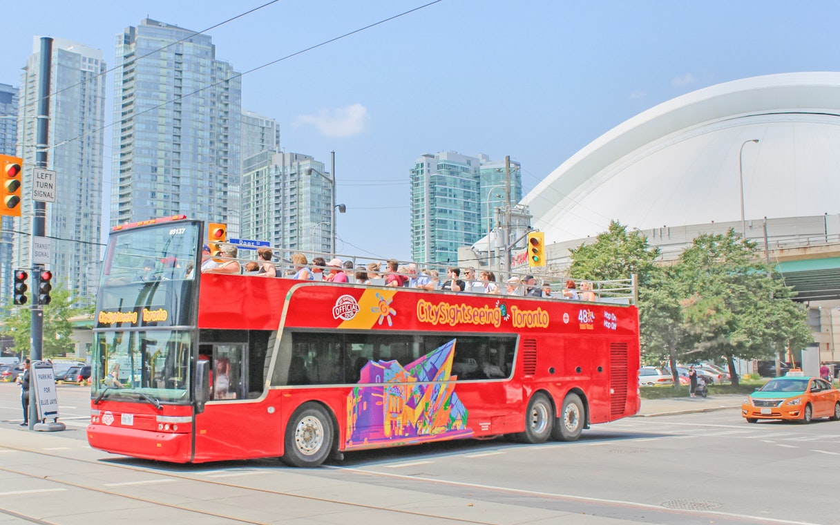 Tourists on a City Sightseeing bus exploring Toronto with CN Tower in the background.