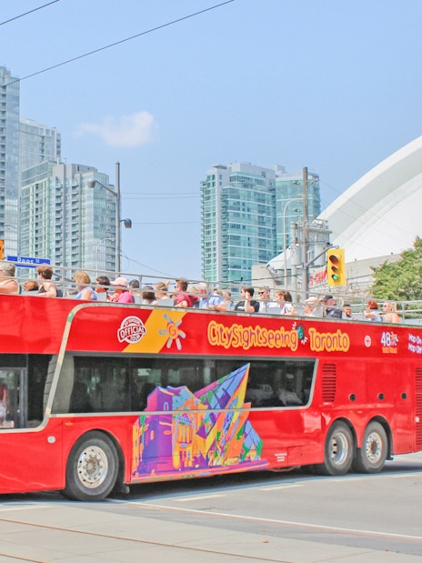 Tourists on a City Sightseeing bus exploring Toronto with CN Tower in the background.