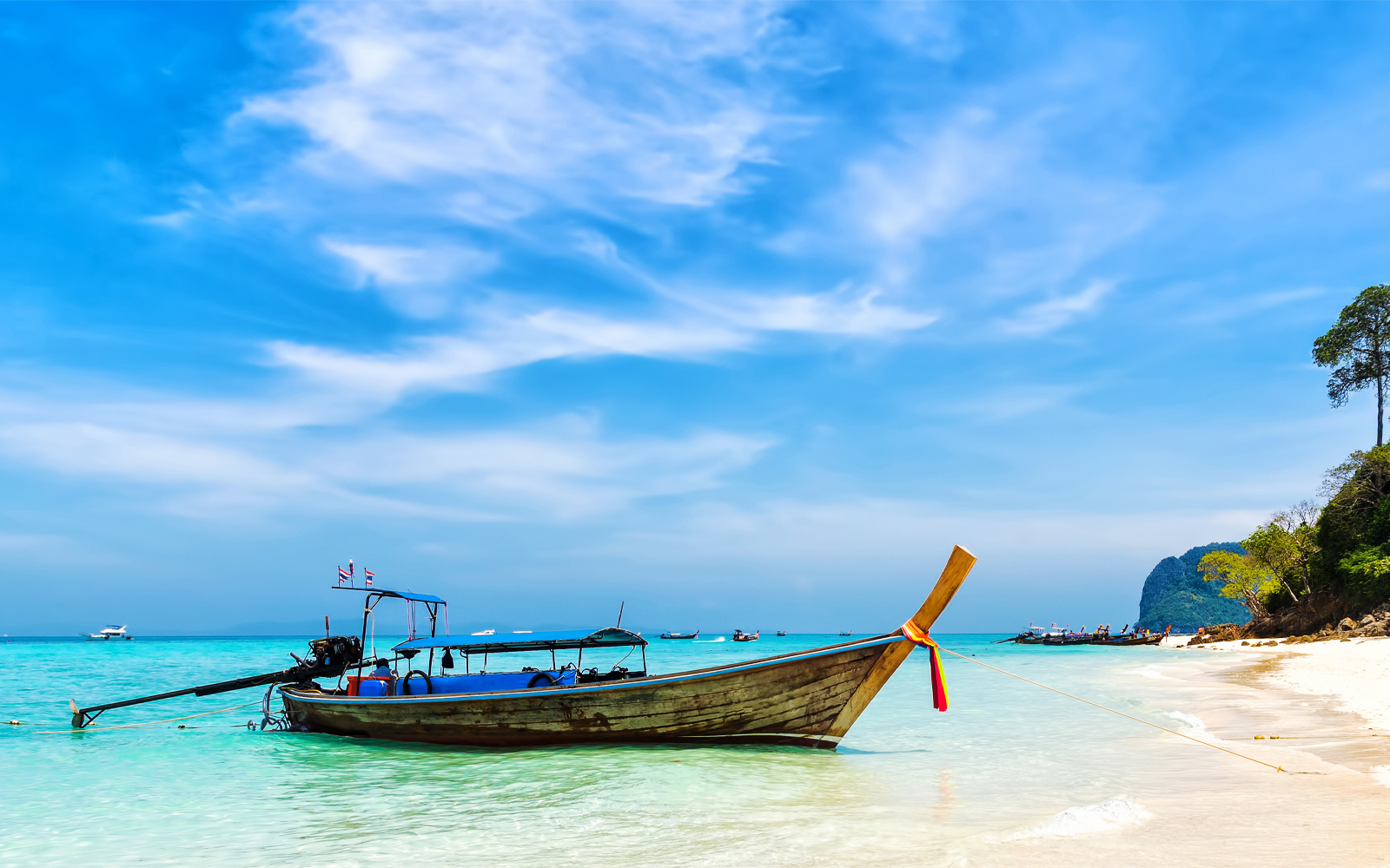 Longtail boat on a sandy beach with clear turquoise water in Thailand.