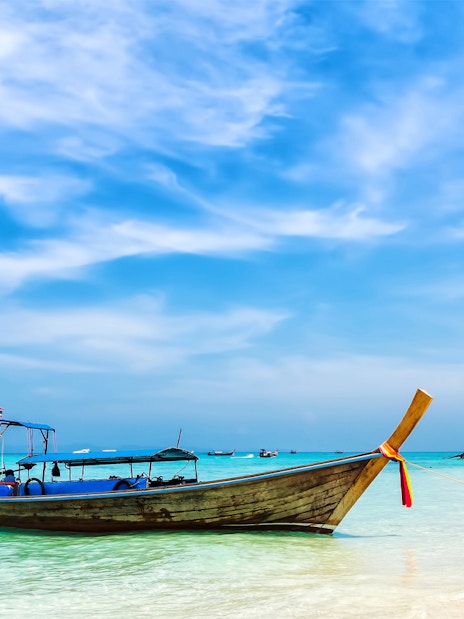 Longtail boat on a sandy beach with clear turquoise water in Thailand.