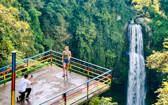 Viewing platform at Curug Cimahi waterfall near Bandung, Indonesia, with lush greenery.