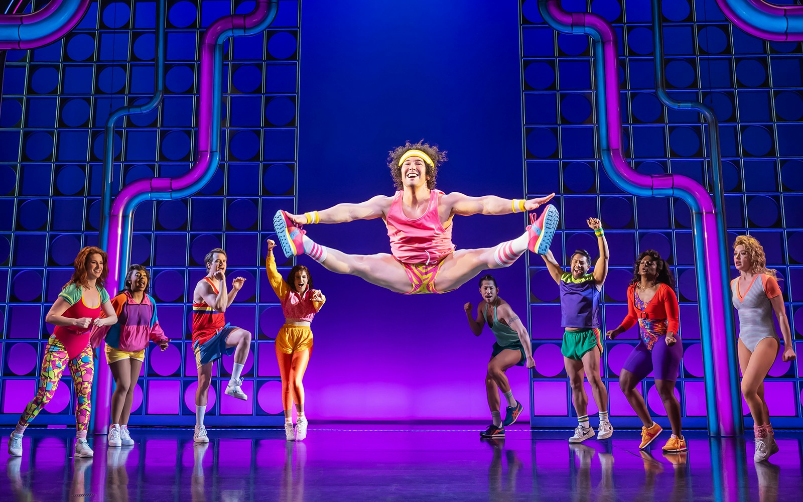 Performers in vibrant workout attire dancing energetically on stage, "The Heart of Rock and Roll" show.