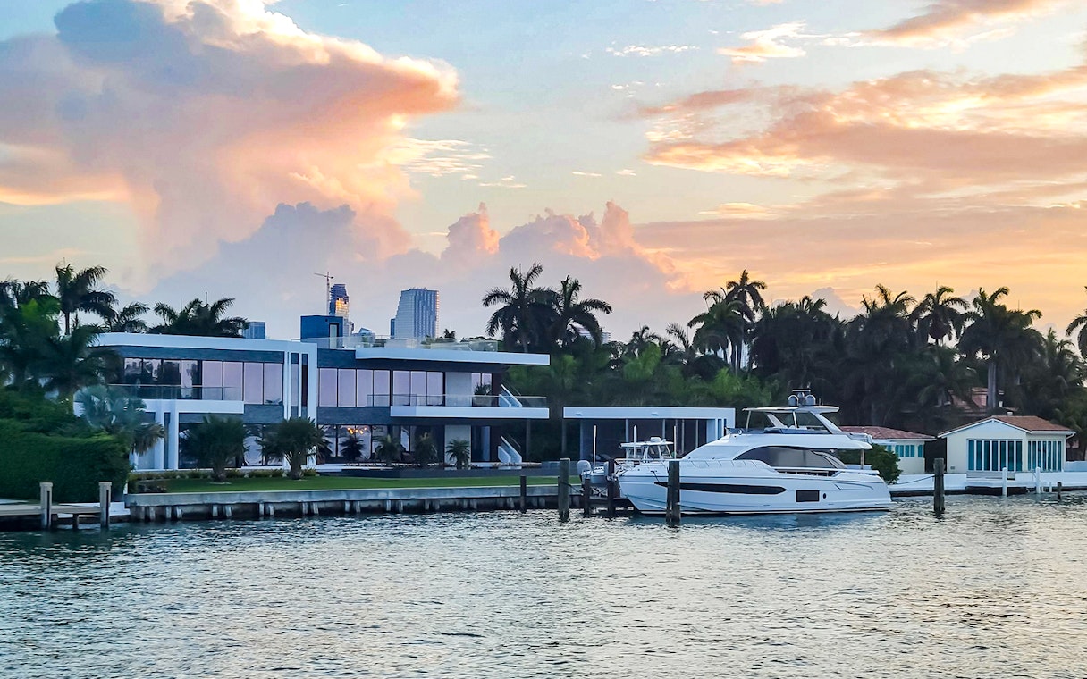 Luxury yacht docked at a waterfront mansion during sunset in Biscayne Bay, South Beach.